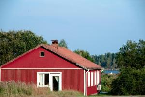 um celeiro vermelho sentado no meio de um campo em Blankaholm nära marinan em Blankaholm