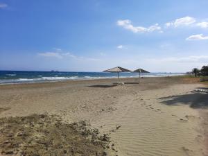 Villa Larnaca Bay Resort في فوروكليني: شاطئ فارغ مع مظلتين والمحيط