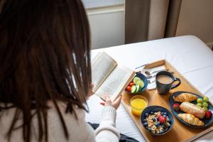 une femme assise à une table avec un livre et un plateau de nourriture dans l'établissement Hotel Olympic Paris Boulogne by Patrick Hayat, à Boulogne-Billancourt