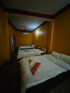 a room with three beds with white sheets and a pillow at Busy Bee Guest House in Sauraha