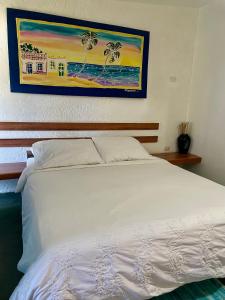 Hotel The Winds Of Margarita في El Yaque: سرير أبيض في غرفة نوم مع لوحة على الحائط