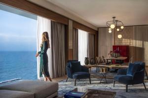 una mujer parada en una sala de estar mirando por la ventana en The David Kempinski Tel Aviv, en Tel Aviv