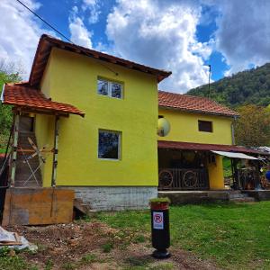 una casa amarilla con una lata de reciclaje delante de ella en STD "Vila Bor" Stara planina en Crni Vrh