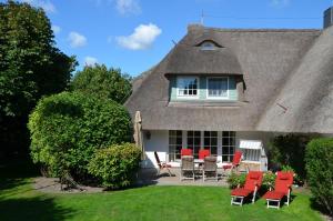 a thatch roofed house with red chairs and a patio at Litzkow 16101 in Archsum