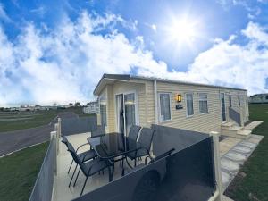 a mobile home with chairs and a table on a porch at Golden Anchor - The Waverley - Coastal Caravan Breaks in Chapel Saint Leonards
