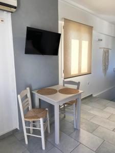 Agnadi Syros Beachfront Studios & Rooms في Megas Gialos - Nites: طاولة بيضاء وكراسي مع تلفزيون على الحائط