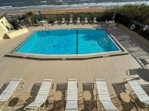 a swimming pool next to chairs and the ocean at Sunrise beach views with top complex amenities and pool access! in Ormond Beach