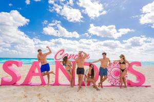 um grupo de pessoas em pé em frente a uma placa na praia em Sandos Cancun All Inclusive em Cancún