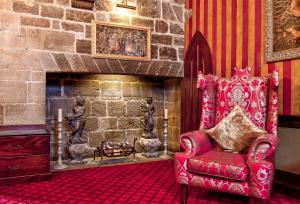 a living room with a red chair and a fireplace at Langley Castle Hotel in Hexham