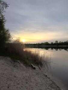 una puesta de sol sobre un cuerpo de agua con hierba en Świetna Chatka, en Świętne