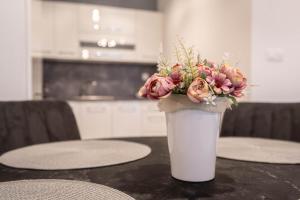 a white vase filled with pink flowers on a table at KARINA APARTMAN in Dunajská Streda