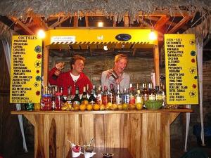 dos hombres parados detrás de una barra con botellas de alcohol en MONTANITA Hugos Place, en Montañita