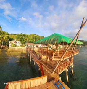 a wooden pier with a green umbrella on the water at CHUE&LARRY'S BEACHSIDE HOMESTAY in Libagon