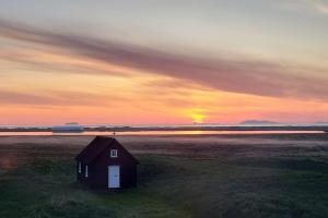 un granero en un campo con la puesta de sol en el fondo en Ibúð með einstöku útsýni en Sauðárkrókur
