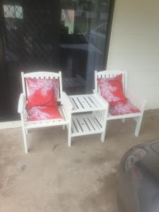 zwei weiße Stühle mit roten Kissen auf einer Veranda in der Unterkunft FRANGIPANI HOUSE in Gladstone