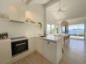 a kitchen with white cabinets and a dining room with the ocean at Sea View Estate - Waiheke Escapes in Onetangi