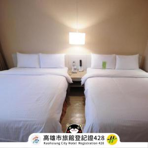 two beds in a hotel room with a table between them at Kindness Hotel - Houyi Jiuru in Kaohsiung