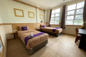 a room with two beds and a desk and windows at Take Guesthouse 1 in Jambi