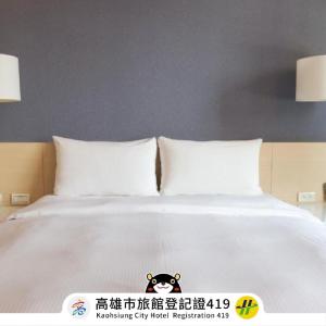 a white bed with two pillows and a dog on it at Kindness Hotel - Kaohsiung Guang Rong Pier in Kaohsiung