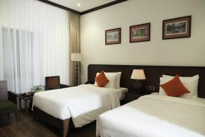 two beds in a hotel room with white and orange pillows at Paul Chabot Hotel in Hai Phong