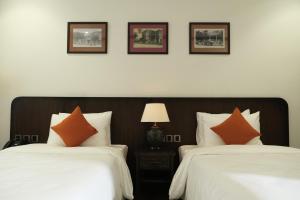 2 łóżka z pomarańczowymi poduszkami w pokoju hotelowym w obiekcie Paul Chabot Hotel w Hajfong