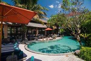 een zwembad in een resort met stoelen en een parasol bij Maca Villas & Spa Bali in Seminyak