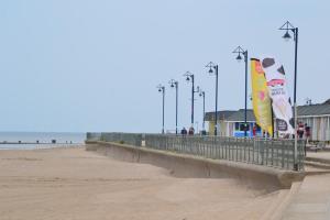 a sandy beach with a pier with flags and lights at Cozzzy Seaside Retreat in Mablethorpe