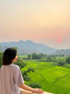 a woman standing on a ledge looking out over a green field at Hiền Hưng Motel - Homestay Bản Lác, Mai Châu in Mai Chau