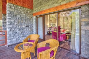 a patio with purple chairs and a stone wall at Span Resort and Spa in Manāli
