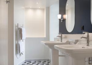 a white bathroom with two sinks and a mirror at Hôtel de la Poste in Beaune