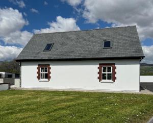 a white house with two windows on a yard at De Búrca Cottage KERRY in Brackhill