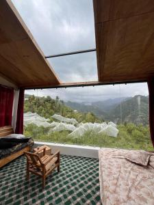 um quarto com uma grande janela com uma cama e uma cadeira em Stargazing Glass Lodge Himachal Pradesh Thachi em Mandi