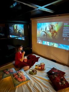 a woman sitting on a bed watching a movie on a screen at Northland Bungalows in Çayırdüzü