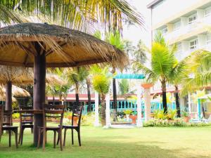 a table and chairs with a straw umbrella and palm trees at Aryana Queen Beach Resort in Wadduwa