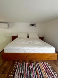 1 dormitorio con cama con sábanas blancas y alfombra en Vourtaréa Guesthouse, en Himare