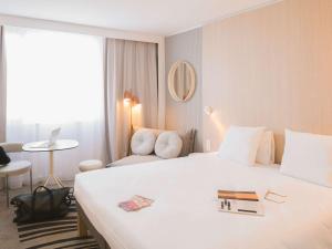 um quarto de hotel com uma grande cama branca e uma cadeira em Novotel Bordeaux Lac em Bordéus