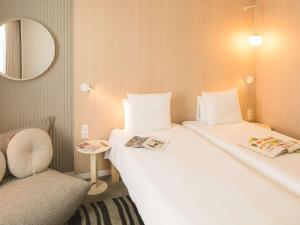 a room with two beds and a chair and a mirror at Novotel Bordeaux Lac in Bordeaux