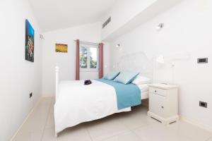 a white bedroom with a bed and a window at Apartments Montevideo in Mali Lošinj