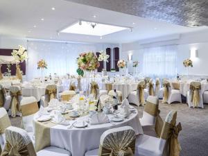 - une salle de banquet avec des tables et des chaises blanches dans l'établissement Mercure Birmingham West Hotel, à West Bromwich