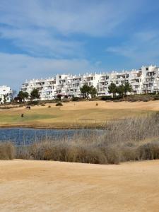 a large white apartment building on a golf course at Luxury Ground Floor Apartment at Golf Resort Condado de Alhama with Private Garden & Pools in El Romero