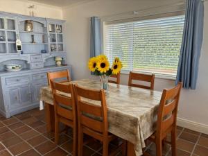 uma mesa de jantar com cadeiras e um vaso de girassóis no topo em Beachcomber Cottages em Ballyconneely