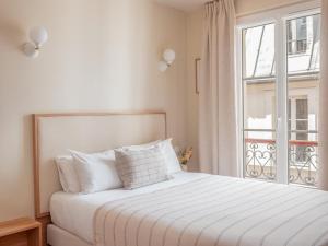 een witte slaapkamer met een bed en een raam bij Hôtel Basss in Parijs