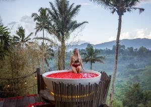 Una donna in bikini seduta in una vasca da bagno di Camaya Bali - Magical Bamboo Houses a Selat