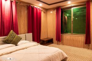 a bedroom with a bed with red curtains and a window at Ghanchi Inn Hotel in Dargai