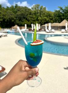 une personne tenant une boisson bleue devant une piscine dans l'établissement La Kawanaise Blue Lagon, à Grand-Bourg