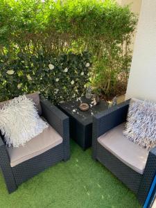two wicker chairs and a table in front of a bush at Appartement cosy in Le Croisic