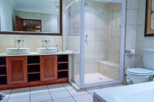 uma casa de banho com um chuveiro, 2 lavatórios e um WC. em RIETONDALE LODGE em Pretoria