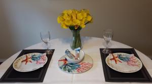 una mesa con dos platos y un jarrón con flores amarillas en Comfy KING Bed, Large private Basement Suite, Smart TV in Penticton- city of PEACHES AND BEACHES en Penticton