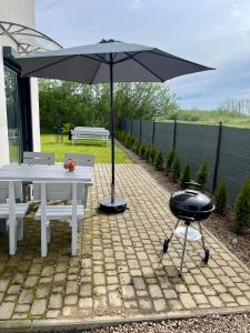 a grill with an umbrella next to a table and bench at Nemo - apartament, domek w Gaskach in Gąski
