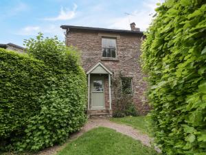 an old brick house is seen through a hedge at Woodlands Cottage in Leominster